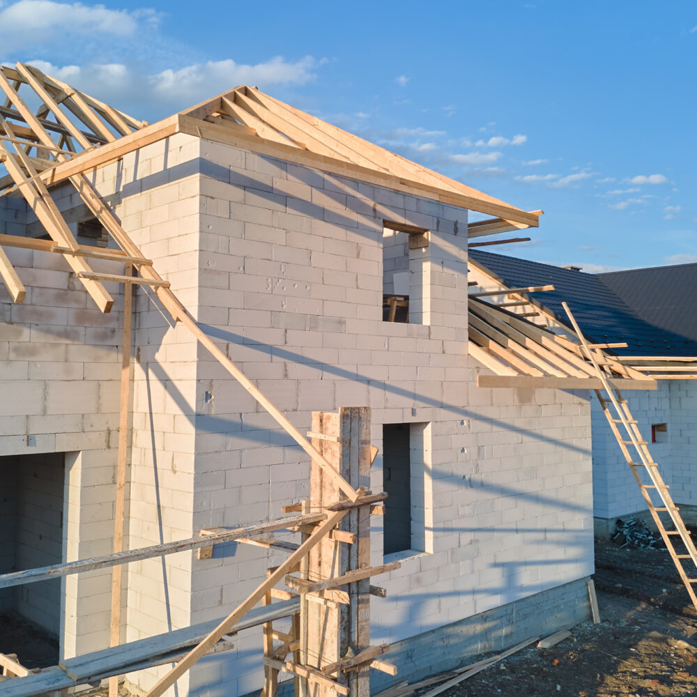 Aerial view of unfinished frame of private house with aerated lightweight concrete walls and wooden roof frame under construction.
