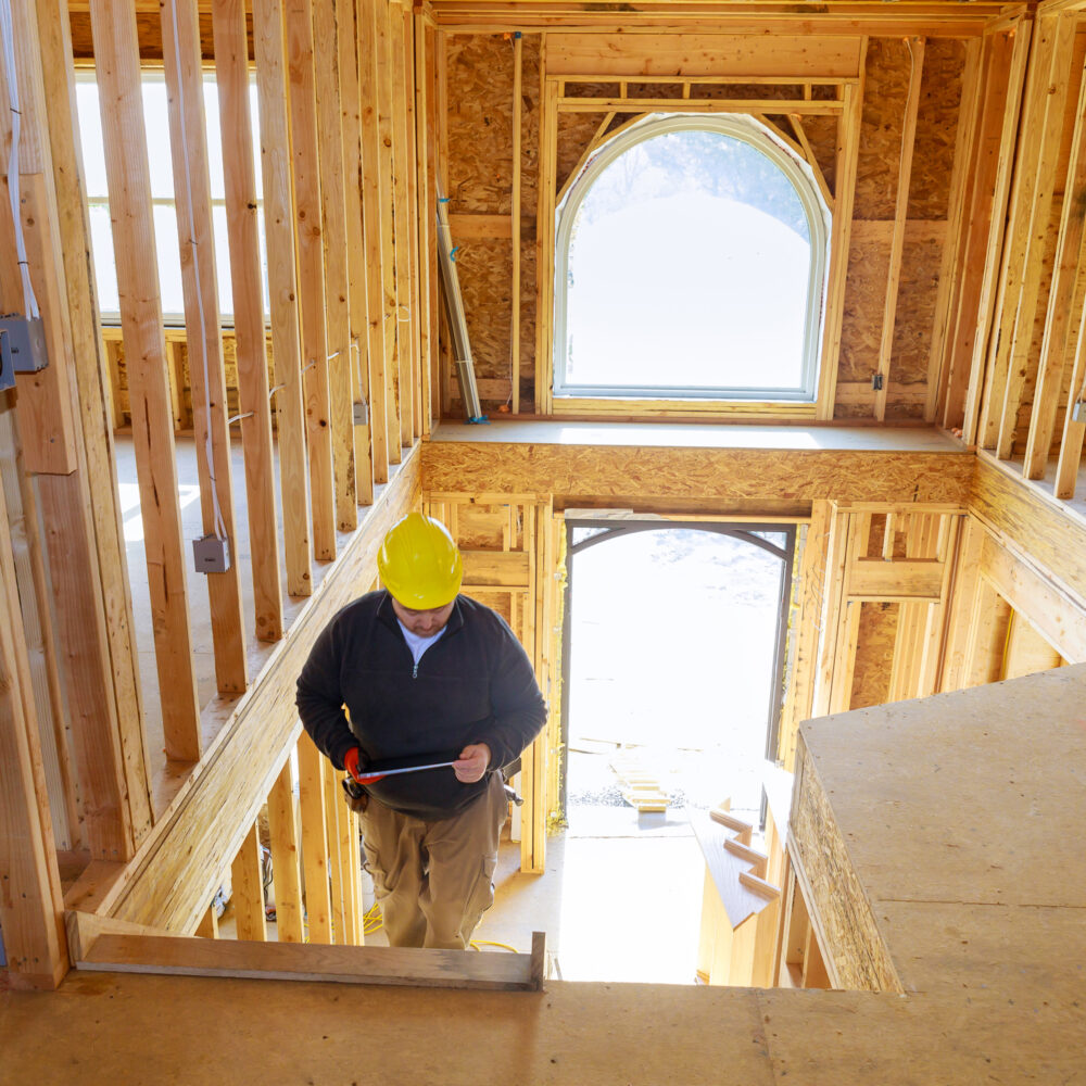Building inspector looking at new home on holding tablet with hard hat