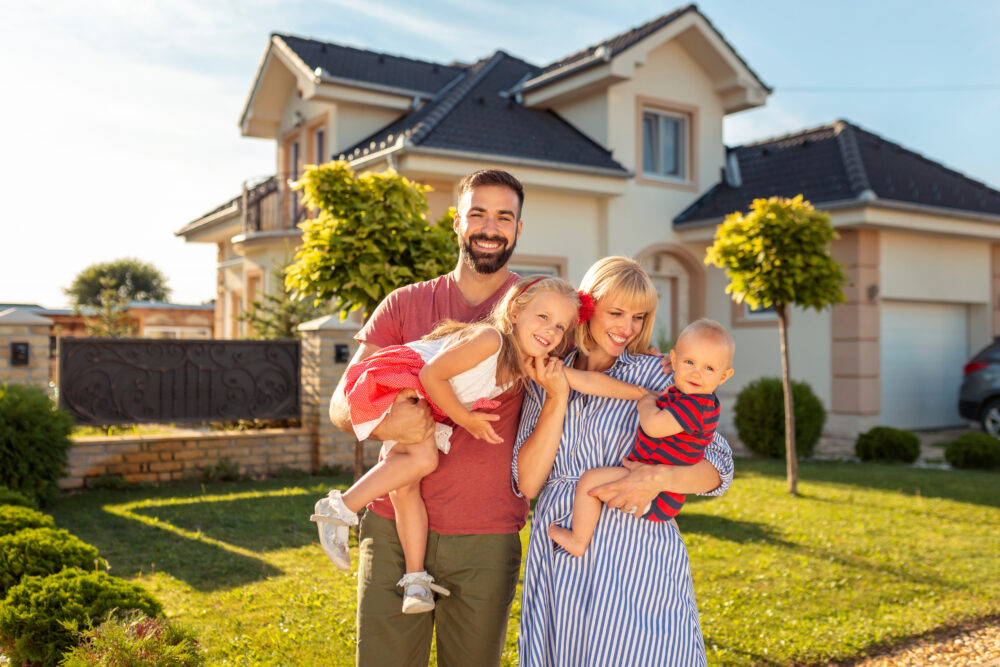 Parents and children having fun standing in front of their new house
