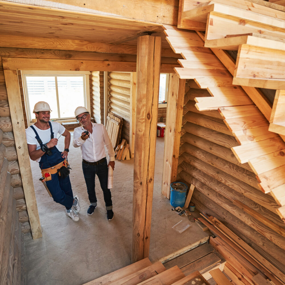 Hopeful construction worker leaning against door and holding nail in hand getting orders from aged site engineer about staircase work